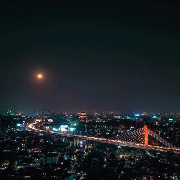 Glimmering city lights compliments the stunning full moon that lights the sky of...