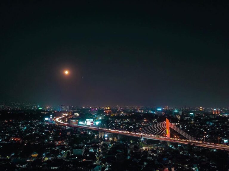 Glimmering city lights compliments the stunning full moon that lights the sky of...