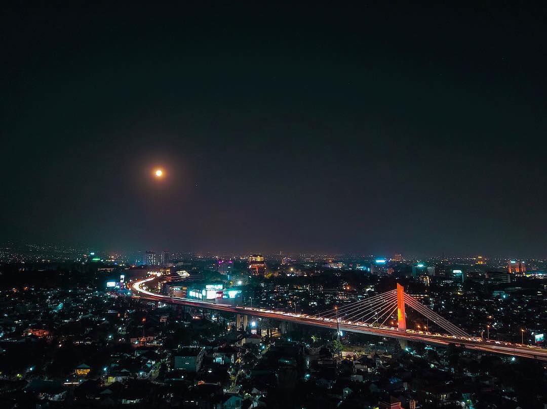 Glimmering city lights compliments the stunning full moon that lights the sky of...